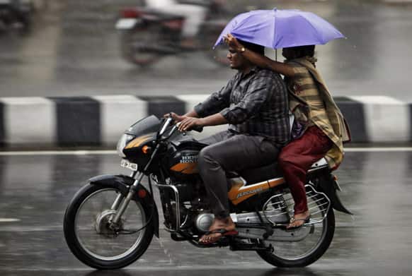 An Indian woman tries to shield her husband on a two wheeler with an umbrella from a heavy monsoon shower in Hyderabad