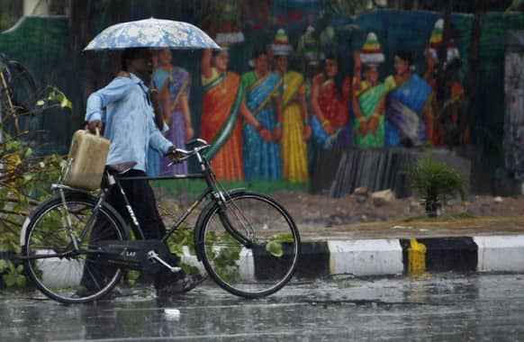 A cyclist and a pedestrian share an umbrella as they walk past a painted wall during sudden rainfall in Hyderabad.
