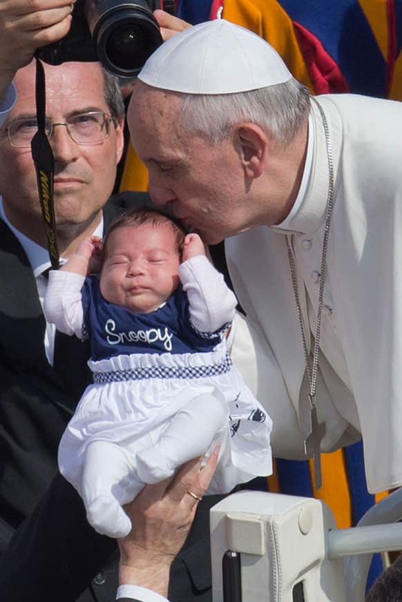 Pope Francis kisses a baby as he arrives in St. Peter`s Square at the Vatican, for his weekly general audience.