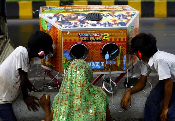 An Indian woman and two boys watch on a traditional biscope, a trailer of the upcoming Bollywood film “Yamla Pagla Deewana 2” in Mumbai.