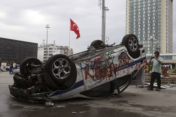 A man using his mobile phone takes a photograph of a destroyed police cars after clashes at the Taskim square in Istanbul.