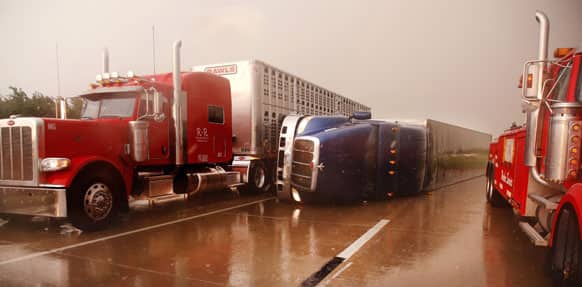 A truck squeezes past an overturned tractor-trailer on I-40 west of Banner Rd., in El Reno, Okla.