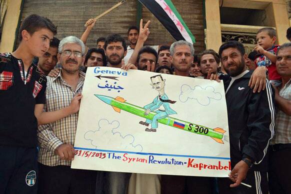 This image provided by Edlib News Network, which has been authenticated based on its contents and other AP reporting, show anti-Syrian regime protesters holding a placard with a sarcastic caricature on it against Syrian President Bashar Assad, during a demonstration, at Kafr Nabil town, in Idlib province.