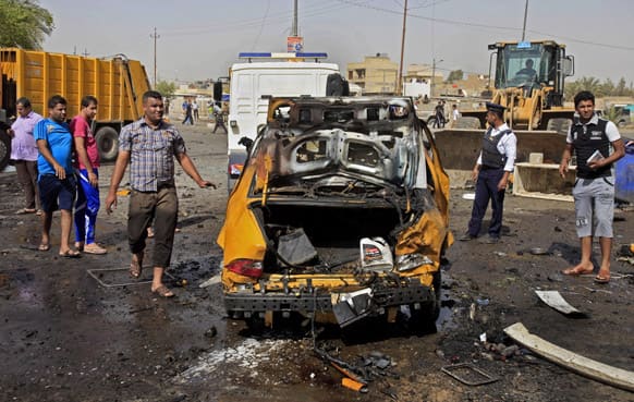 Iraqis inspect the scene of a bomb attack at Sadr City in Baghdad, Iraq. A bomb left on a Baghdad minibus and a suicide truck bomb north of the Iraqi capital killed and wounded dozens of people, on Tuesday, officials said.