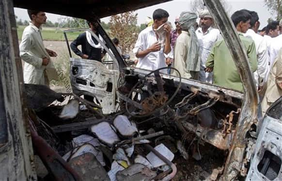 Pakistanis gather by the wreckage of a minibus, which was burnt after gas cylinder explosion, in Gujrat, Pakistan. Police say that a teacher was among more than a dozen people burned to death in eastern Pakistan when a minibus taking children to school suddenly caught fire.