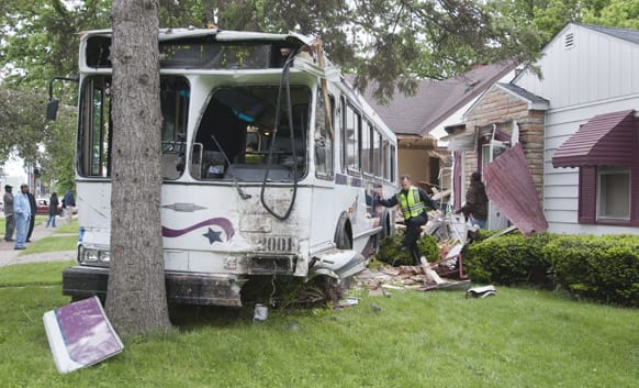 A Saginaw police officer climbs through the rubble as a STARS bus sits on the lawn of a house in Saginaw after it collided with a minivan and heavily damaged two houses before hitting a tree on Friday morning.