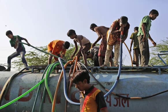 An Indian girl sucks on a hose to pull water as she stand on top of a government tanker delivering drinking water because of short supply in running water taps at a slum in New Delhi.