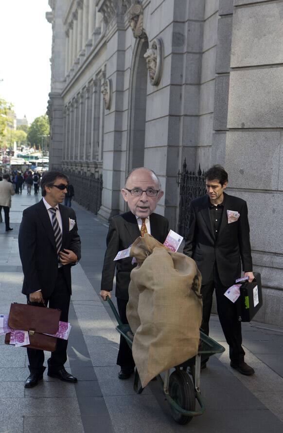 A man wearing a mask representing Spain`s finance minister Cristobal Montoro stages a protest with others while symbolically delivering sacks of cash from the Bank of Spain, seen in background to an already rescued Spanish bank in Madrid.