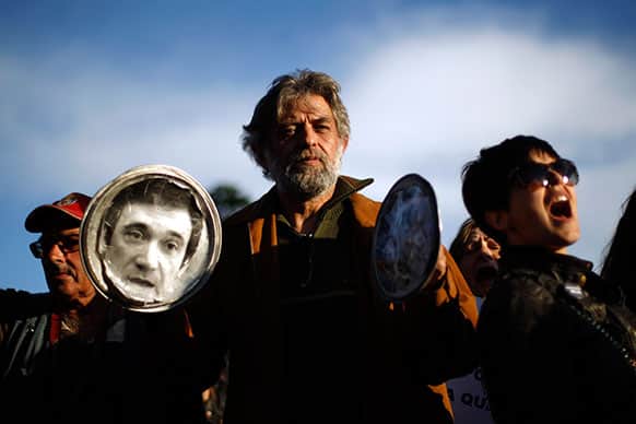 A man bangs pot lids, one of them with the photograph of the Portuguese Prime Minister Pedro Passos Coelho, as others shout slogans during a protest outside Lisbon`s Belem presidential palace where a meeting of the State Council is taking place.