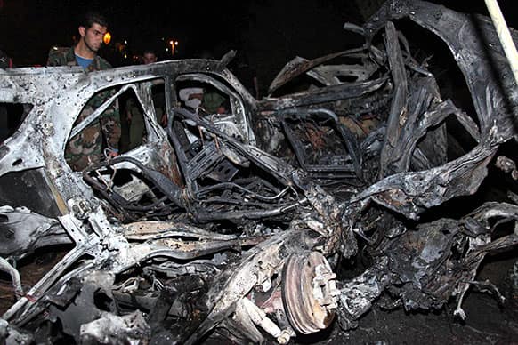 This photo released by the Syrian official news agency SANA, claims to show a Syrian army soldier inspecting a damaged car at the scene of a car bomb which exploded, in Damascus, Syria.