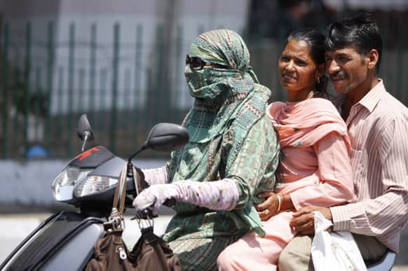 A couple rides pillion behind a woman with her face covered to protect herself from the heat, in Jammu.