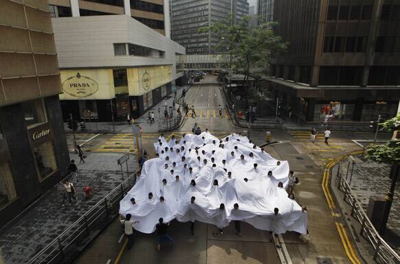 Participants, with their heads sticking out from holes of a large white fabric, perform during a performance,