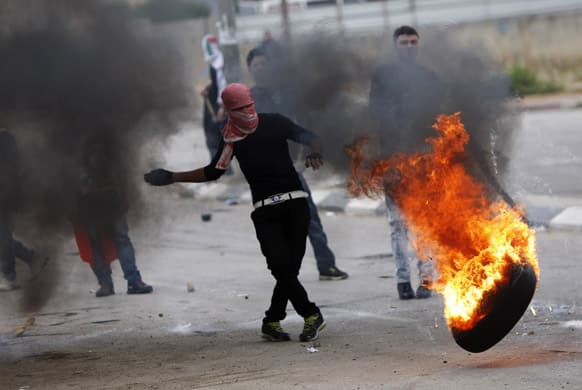 A masked Palestinian kicks a burning tire during clashes after a rally marking Nakba Day outside Ofer, an Israeli military prison near the West Bank town of Ramallah.