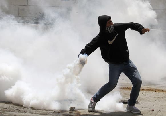 A masked Palestinian throws back a tear gas canister during clashes after a rally marking the Nakba Day outside the West Bank town of Hebron. Palestinians annually mark the