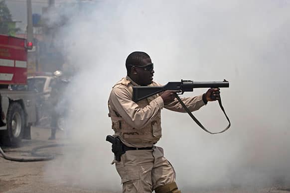 A police officer aims a tear gas gun at protestors demonstrating against the government of Haitian President Michel Martelly, near the sight where Martelly is expected to deliver a speech marking his two years in office, in Port-au-Prince, Haiti.
