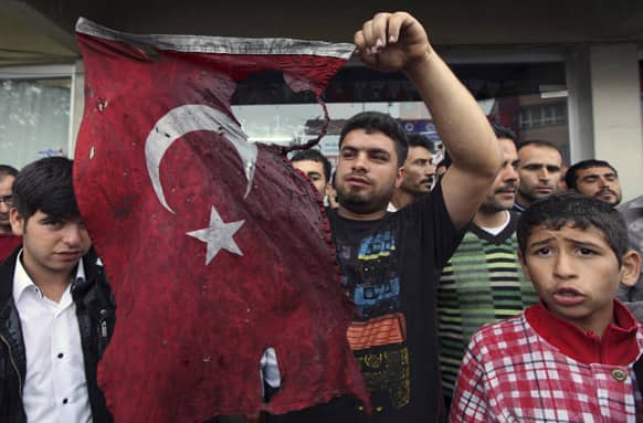 Turkish people display a damaged national flag found in the debris of a destroyed shop as they stage an anti-government protest near the scene at one of the Saturday explosion sites that killed 46 and injured about 50 others, in Reyhanli, near Turkey`s border with Syria.