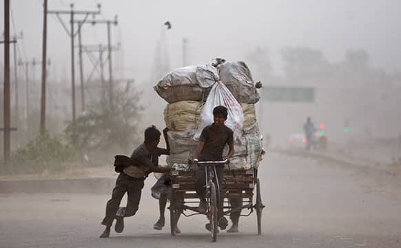 A ragpicker pedals a loaded cart as others help by pushing it on a road during a dust storm in Jammu.