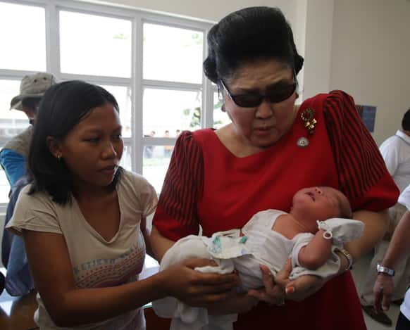 Former Philippine First Lady Imelda Marcos, right, reacts as she carries a baby at a