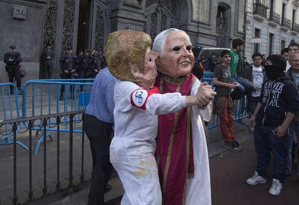 Protesters with masks depicting German Chancellor Angela Merkel and Pope Francis, dance in front of the Education Ministry during a protest march in Madrid, Spain.