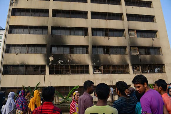 Workers stand outside an 11-story building that houses the Tung Hai Sweater Ltd. factory and apartments after a fire in Dhaka, Bangladesh.