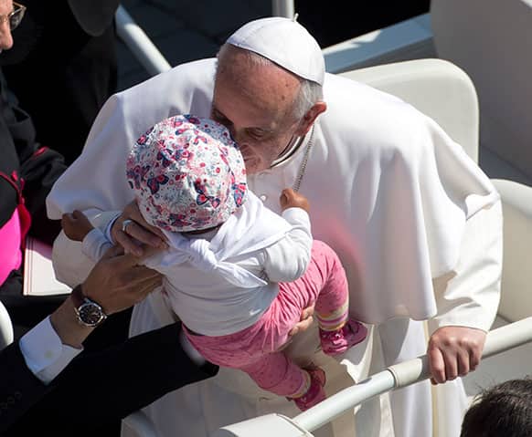 Pope Francis kisses a baby as he arrives in St. Peter`s Square at the Vatican for his weekly general audience.