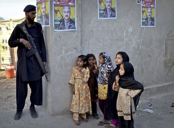 Pakistani children look at a soldier standing guard at an entrance of a compound where an election rally is held in Quetta, Pakistan.