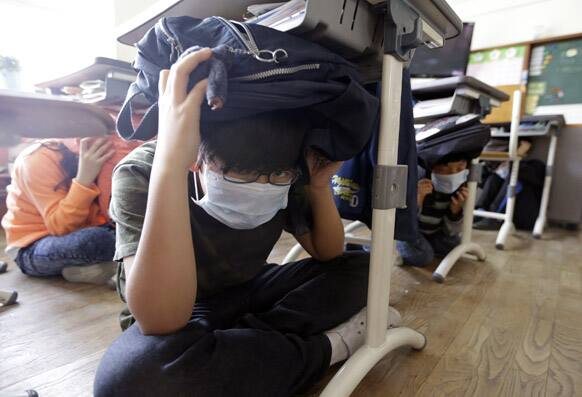 South Korean elementary school students, with schoolbags on their heads, crouches under a desk during an earthquake drill in Seoul.