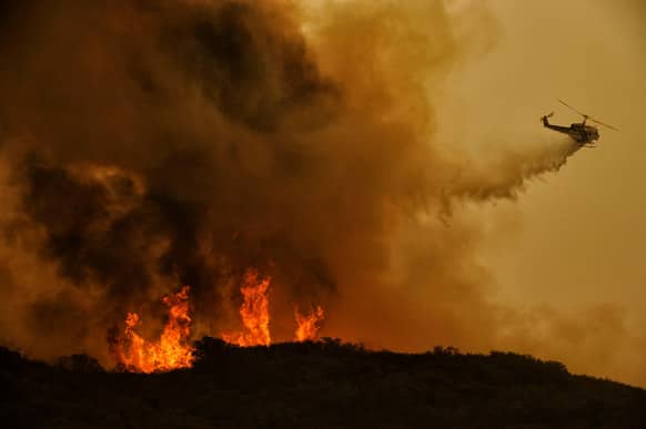 A firefighting helicopter makes a drop on a wildfire in Thousand Oaks, Calif. A huge Southern California wildfire burned through coastal wilderness to the beach on Friday then stormed back through canyons toward inland neighborhoods when winds reversed direction.