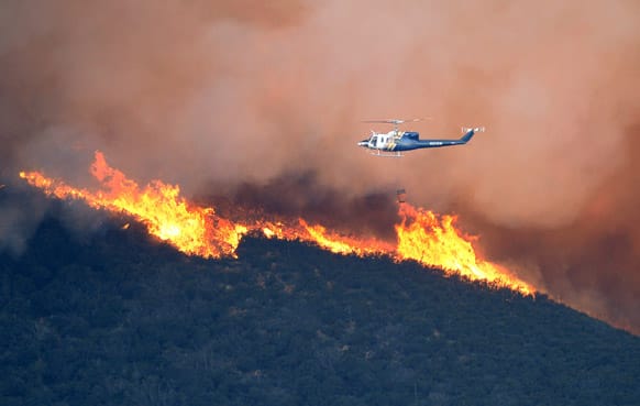 A water dropping helicopter gets ready to make a drop on a fire burring in Point Mugu State Park during a wildfire that burned several thousand acres in Ventura County, Calif.