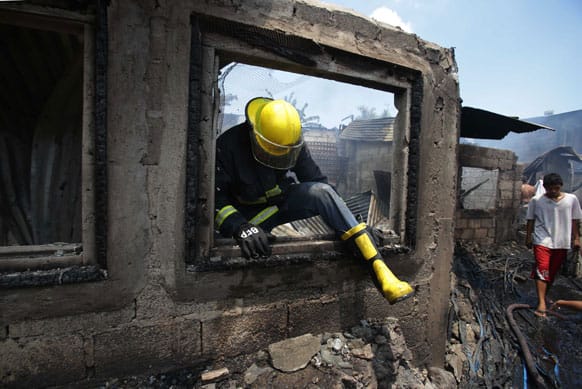 A fireman comes out the window of a burned house after it caught fire together with about 100 homes in suburban Quezon city, north of Manila, Philippines.