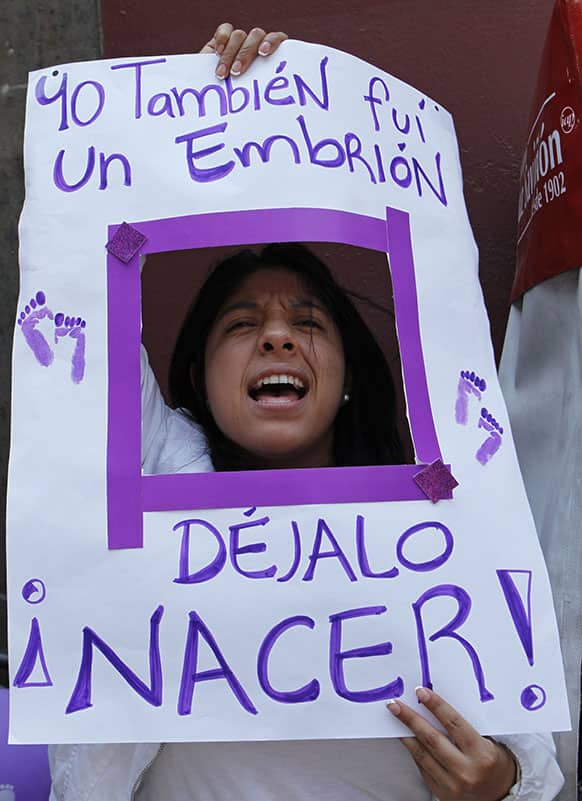 An anti-abortion activist yells through a poster that reads in Spanish