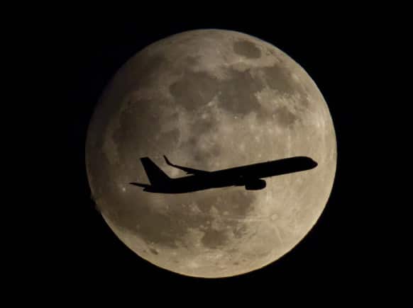 A passenger airplane is about to land at the airport in Frankfurt, Germany, thereby passing the moon which is clearly visible at night.