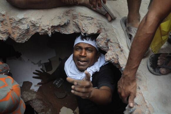 A Bangladeshi rescuer looking for survivors gestures from beneath a concrete slab of a building that collapsed Wednesday in Savar, near Dhaka, Bangladesh.