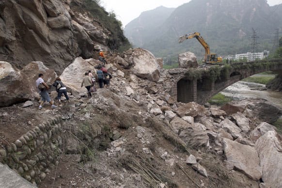 This photo released by China`s Xinhua News Agency, people walk on rocks fallen due to a landslide triggered by a strong quake in Baosheng Township, Lushan County, southwest China`s Sichuan Province.