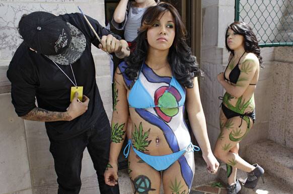 Tattoo artist Robert Duran touches up performer Ashley Lucero with a marijuana-themed body paint design, as Vanessa Pacheco looks on at right, at the Denver 4/20 pro-marijuana rally at Civic Center Park in Denver.