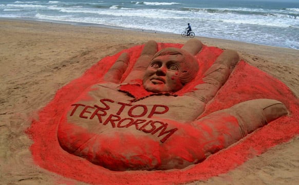 A cyclist pedals past a sculpture with a message against terrorism, created after attacks in Boston and Bangalore, at the golden sea beach in Puri.