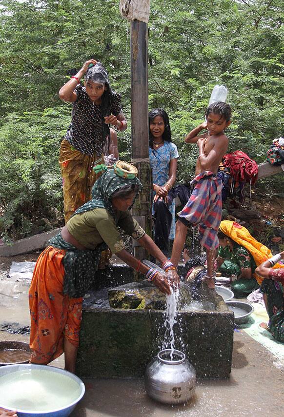 An Indian woman fetches drinking water from a leaking pipe as others bathe under it on the outskirts of Gandhidham in the Kutch district of Gujarat state.