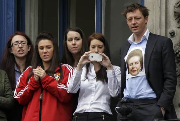 An office worker wearing a depiction of former British Prime Minister Margaret Thatcher on his shirt, and others watch the ceremonial funeral procession for the former prime minister from an office balcony in central London.