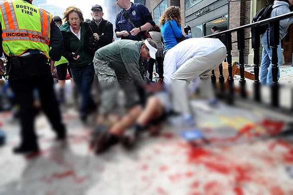 An injured person is helped on the sidewalk near the Boston Marathon finish line following an explosion in Boston.