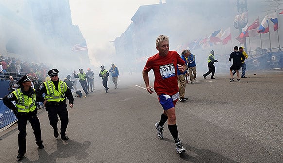 A Boston Marathon competitor and Boston police run from the area of an explosion near the finish line in Boston.
