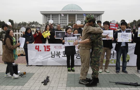 Anti-war activists wearing military clothes of a North, left, and South Korea hug each other during a rally to mark Global Day of Action on Military Spending in front of the National Assembly in Seoul, South Korea.