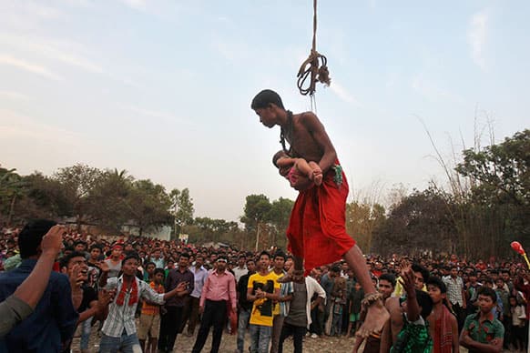 A Bangladeshi Hindu devotee carries a child as he hangs in a rope with hooks pierced in his back as part of a ritual during the Charak Puja festival in Dhaka, Bangladesh.
