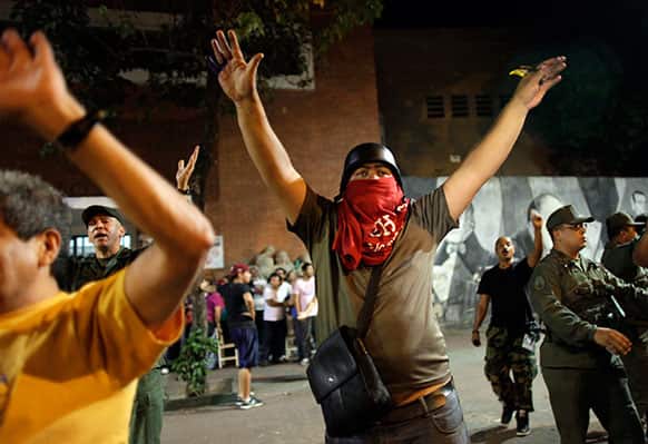 Chavista militants and soldiers try to calm down a group of government supporters as opposition supporters take cover in the background, outside a a polling station that closed after remaining open about 20 minutes past the allotted time, in Caracas, Venezuela.