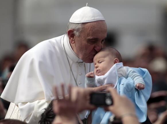 Pope Francis kisses a baby as he is driven through the crowd with his popemobile in St. Peter`s Square prior to the start of his weekly general audience at the Vatican.