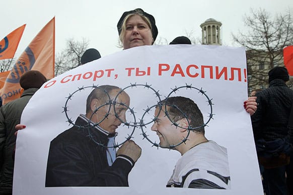 A demonstrator holds a poster showing Russian President Vladimir Putin, left, and Prime Minister Dmitry Medvedev overlayed with the Olympic rings in barbed wire, and meaning that preparations for the Sochi Games is used for fraud and money laundering, during an opposition rally in Moscow.