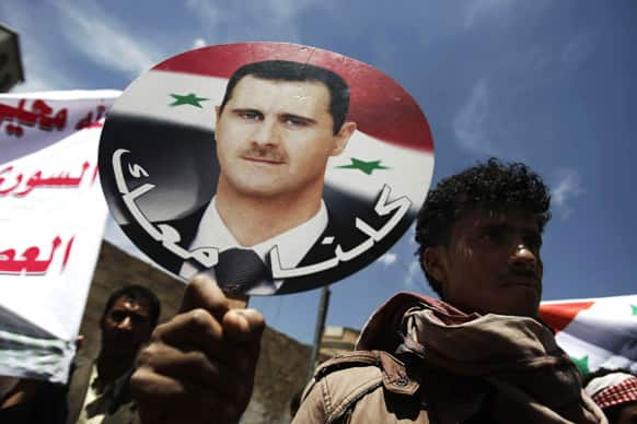 A Yemeni man holds a placard of Syrian president Bashar Assad, with Arabic that reads,