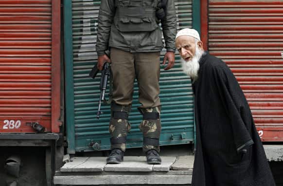 An elderly Kashmiri man walks past an Indian paramilitary soldier standing guard at a closed market during a strike in Srinagar.