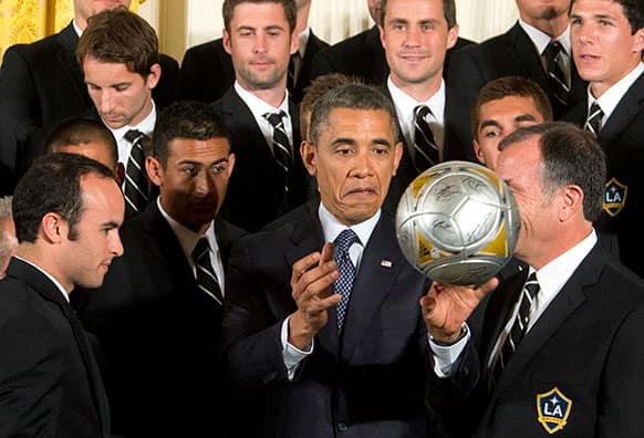 President Barack Obama, center, flanked by LA Galaxy forward Landon Donovan, left, and coach Bruce Arena, right, throws the soccer ball to the crowd during a ceremony in the East Room of the White House in Washington.