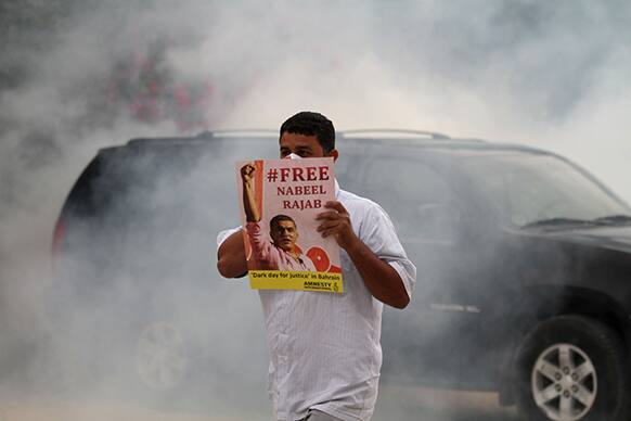 A Bahraini anti-government protester holds a poster as riot police, unseen, fire tear gas outside the home of jailed human rights activist Nabeel Rajab in Bani Jamra, Bahrain.
