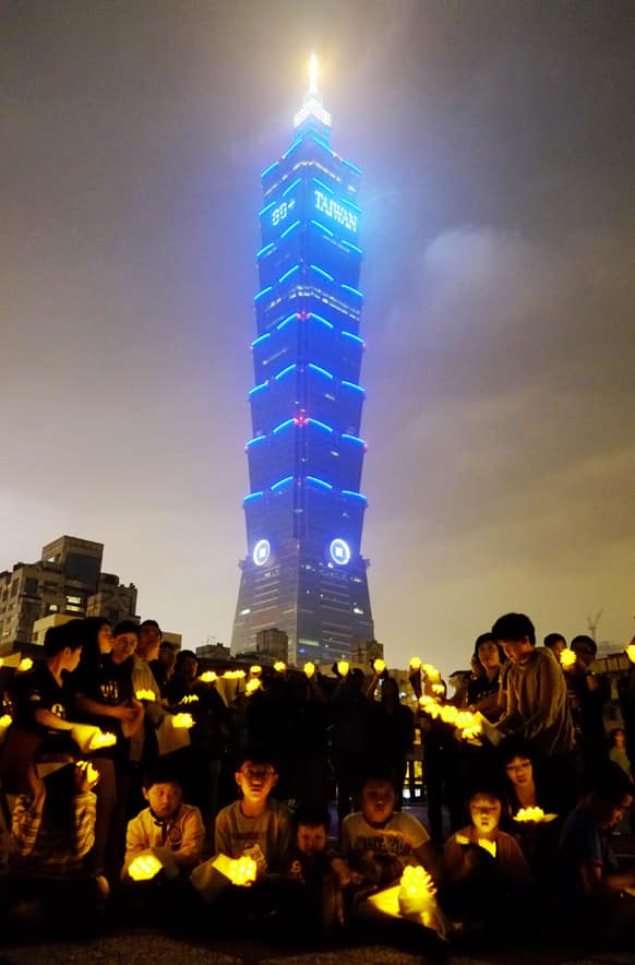 Children turn on their LED lights moments before Taipei 101 building turns its lights off to observe international